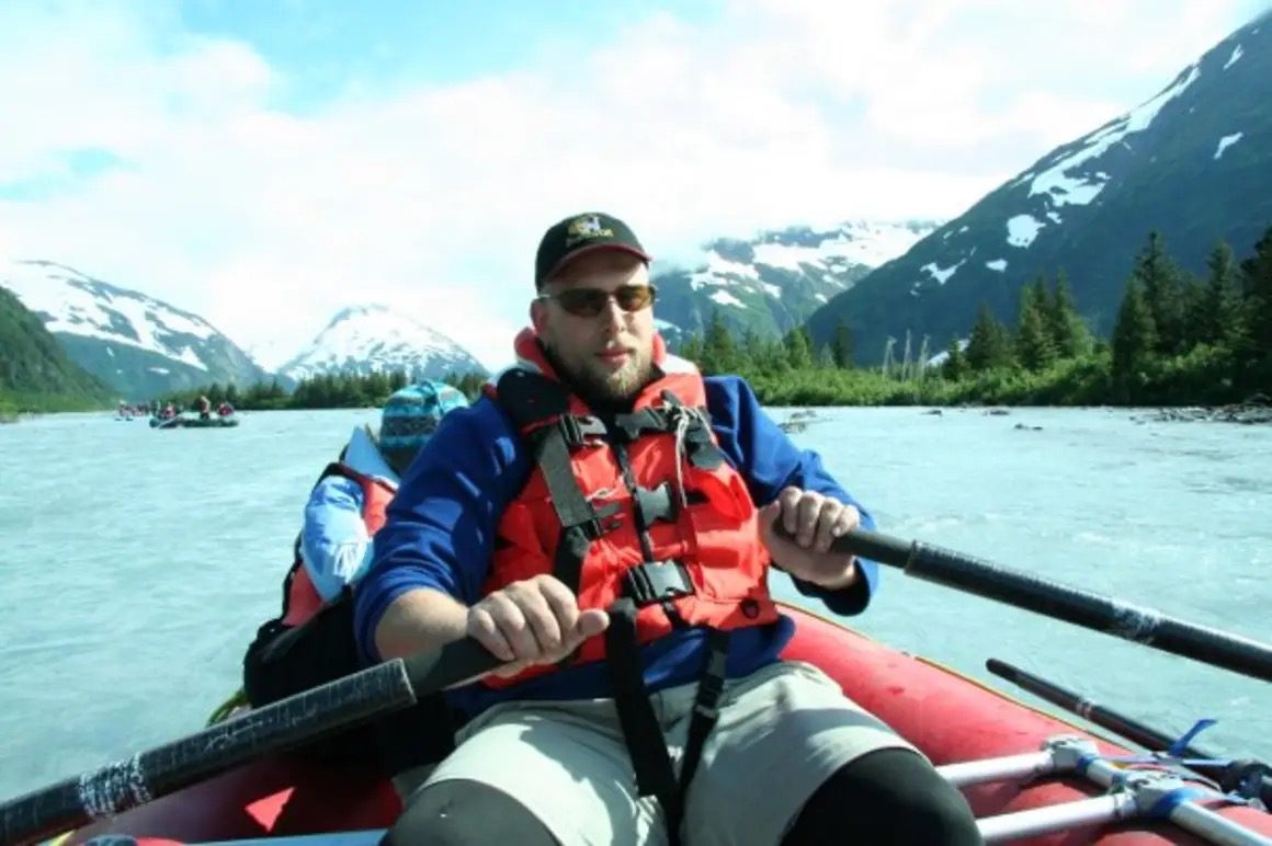Instructor in a life jacket rowing a raft on a glacial Alaska river during safety training