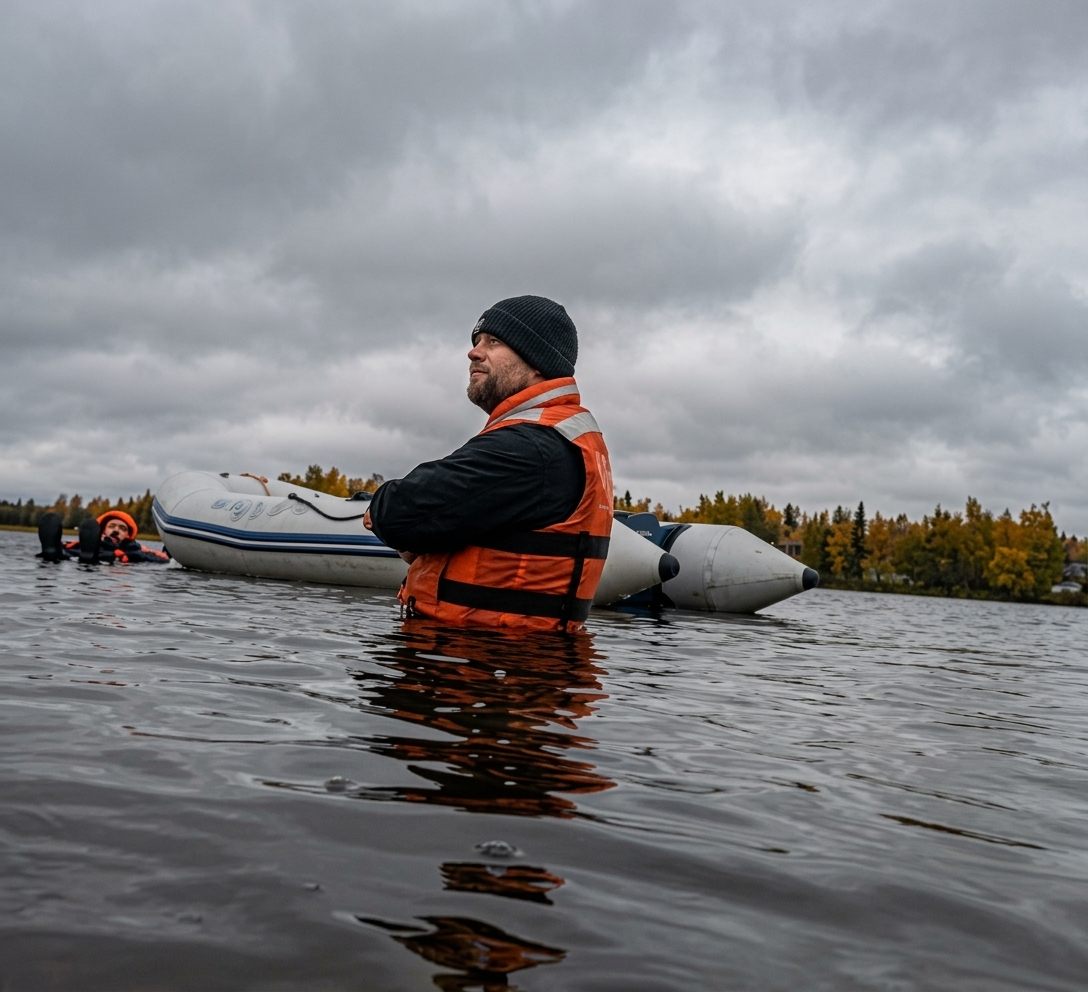 Instructor in an orange life vest standing in a lake beside an inflatable boat during water safety training